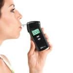 A woman blowing through a breathalyser that shows the result