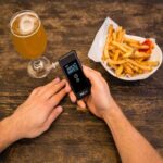 A person holding a breathalyser next to food and alcoholic beverage