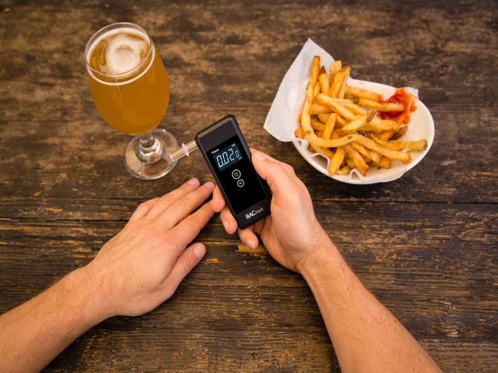 A person holding a breathalyser next to food and alcoholic beverage