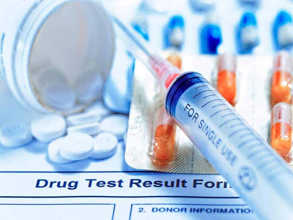 Drug test result form, pills, and syringe