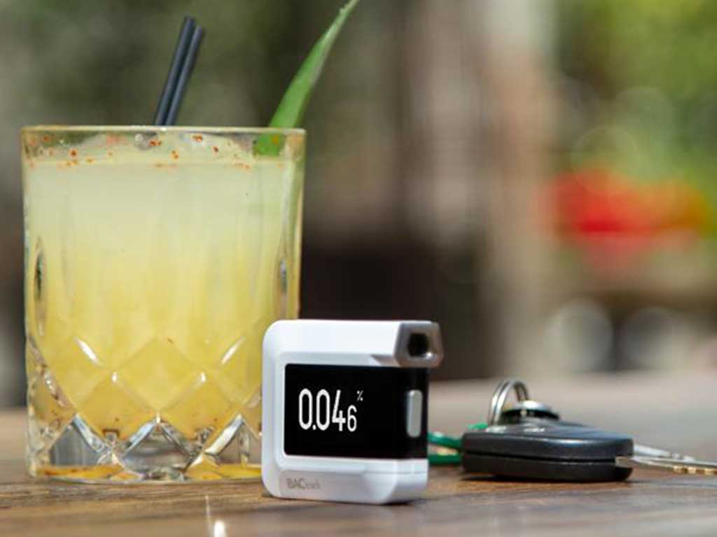 A breathalyser and a glass of alcoholic drink in the background