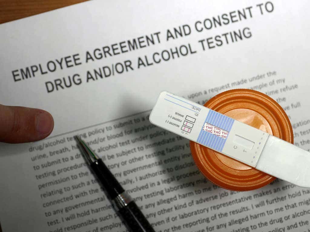 A drug and alcohol testing consent form with a pen and testing kits.
