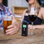 A man and woman drinking alcohol with a breathalyzer ready for monitoring