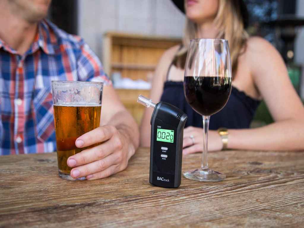 Two individuals enjoying alcoholic beverages with a breathalyser visible on the table
