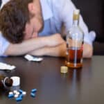 A man sleeping with pills and alcohol bottle on the table