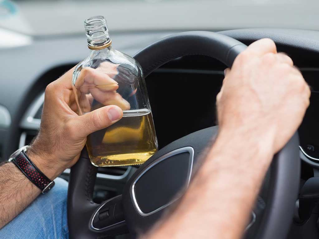 A person holding a bottle of alcohol while driving.