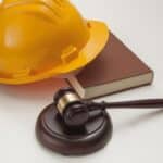 A hard hat on a book next to a gavel on a soundblock