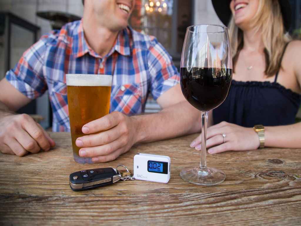 A man and a woman are drinking together with a breathalyser on the table.