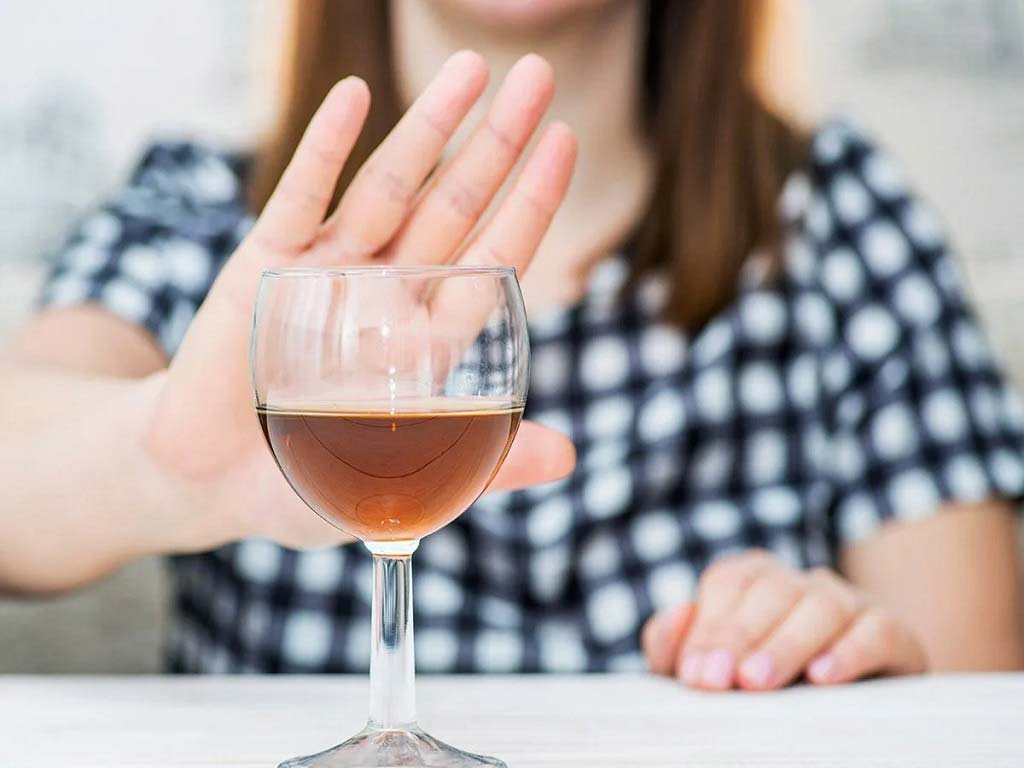 A woman gesturing no to a glass of alcohol