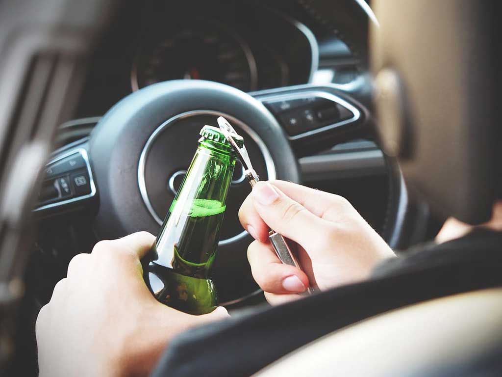 A person driving while opening a bottle of alcohol