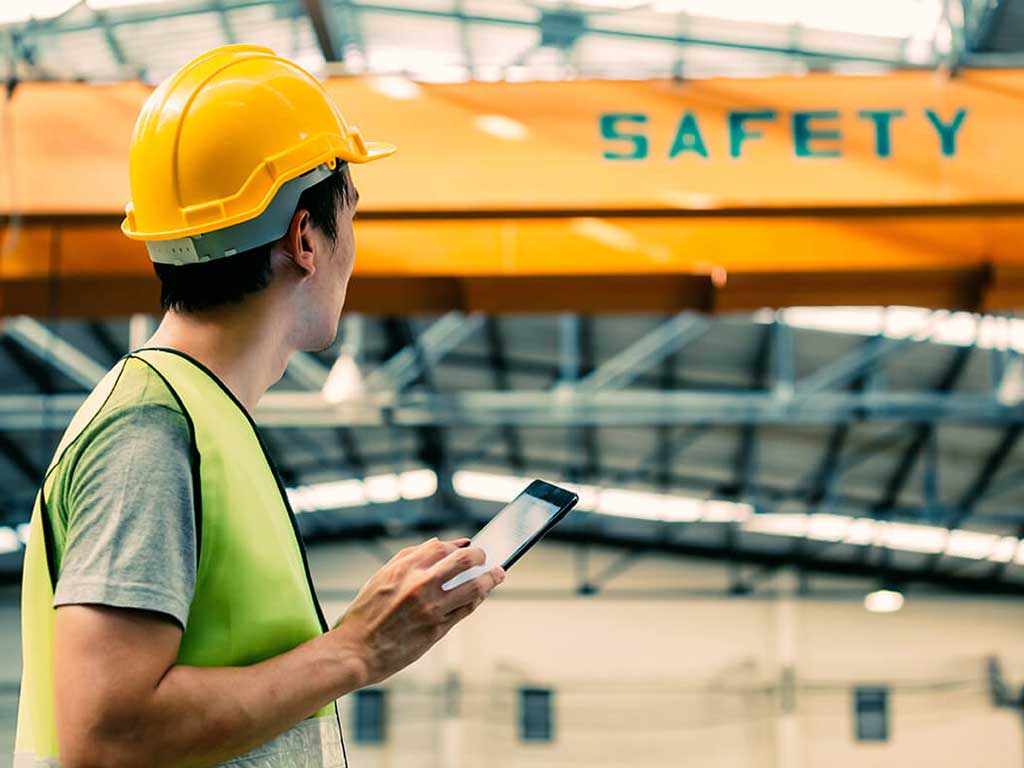 An employee in a work environment wearing a protective hard hat and holding a mobile device.