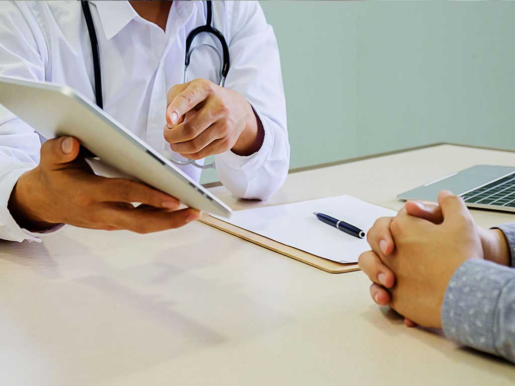 A health professional talking to a patient while pointing at his tablet computer