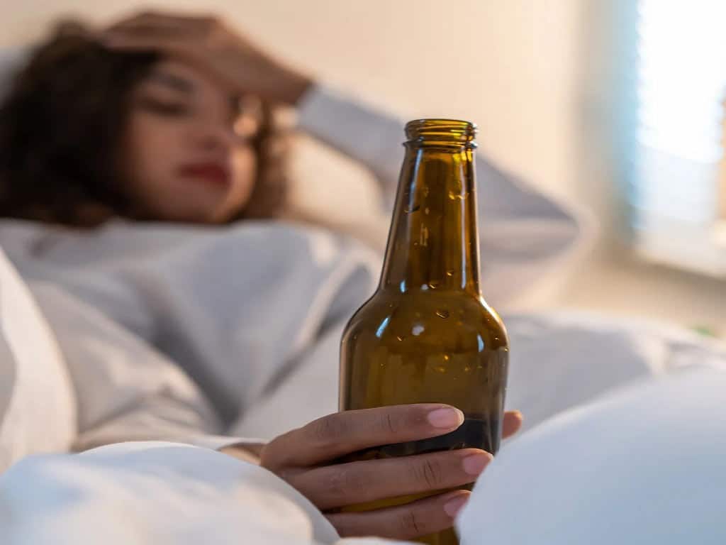 A woman lying on bed while holding a bottle of beer