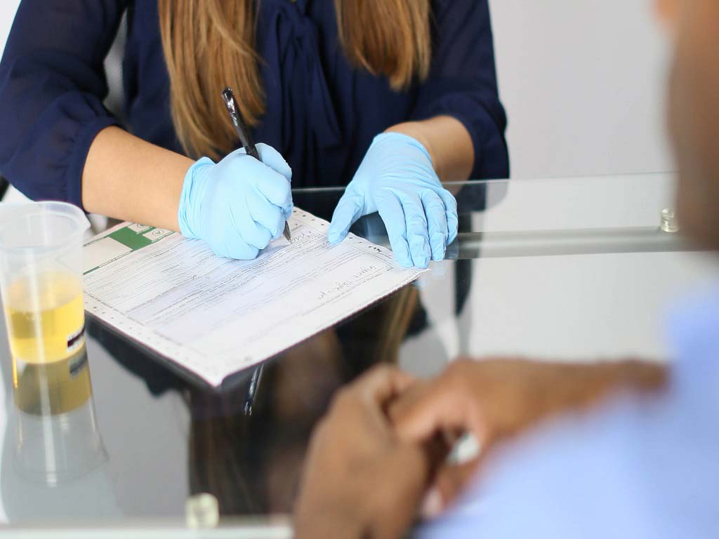 A woman filling out a form with a urine sample next to her