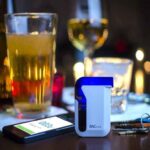 A breathalyser, smartphone, keys, and glass of drink on the table