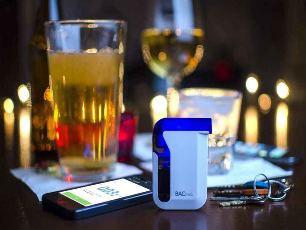 A breathalyser, smartphone, keys, and glass of drink on the table