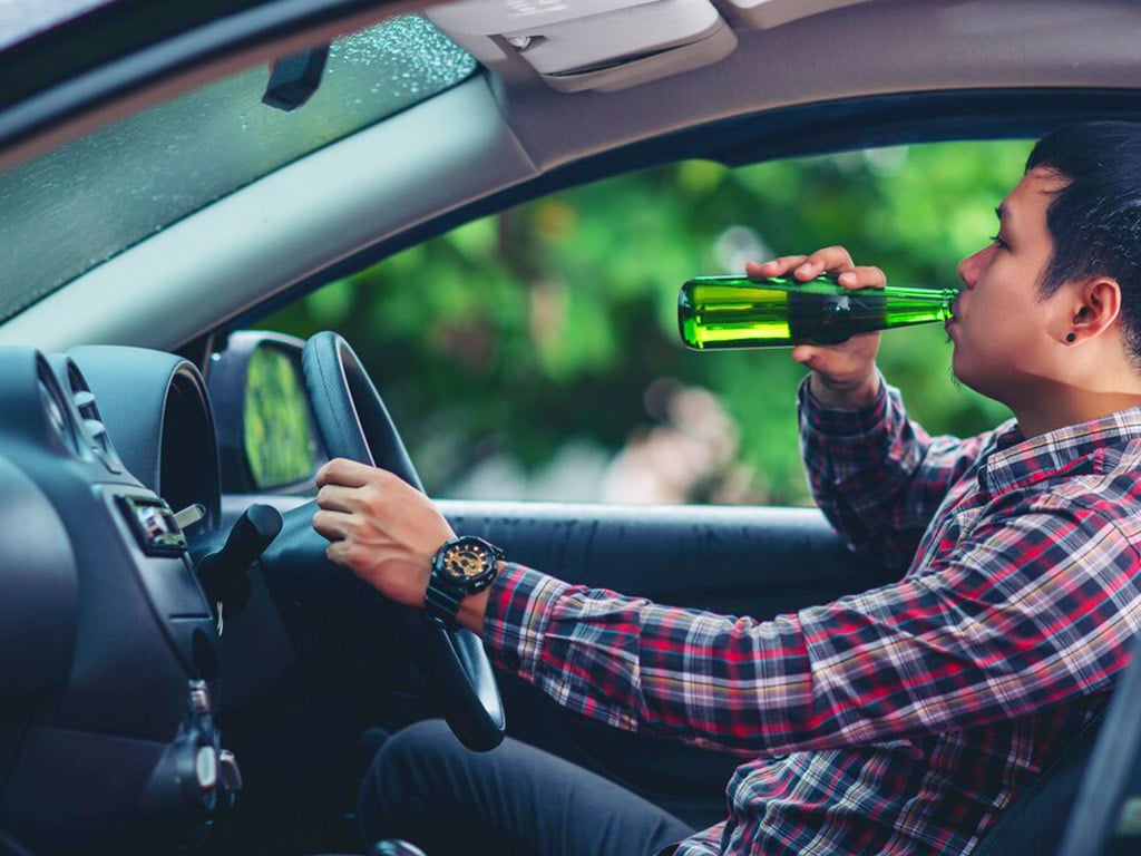 A man drinking alcohol from a bottle while driving