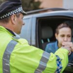 A police officer conducting a roadside breath test on a woman inside a car