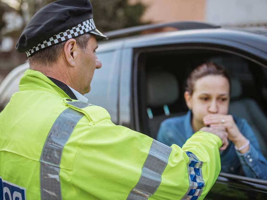 A woman blowing into a breath tester held by a police officer