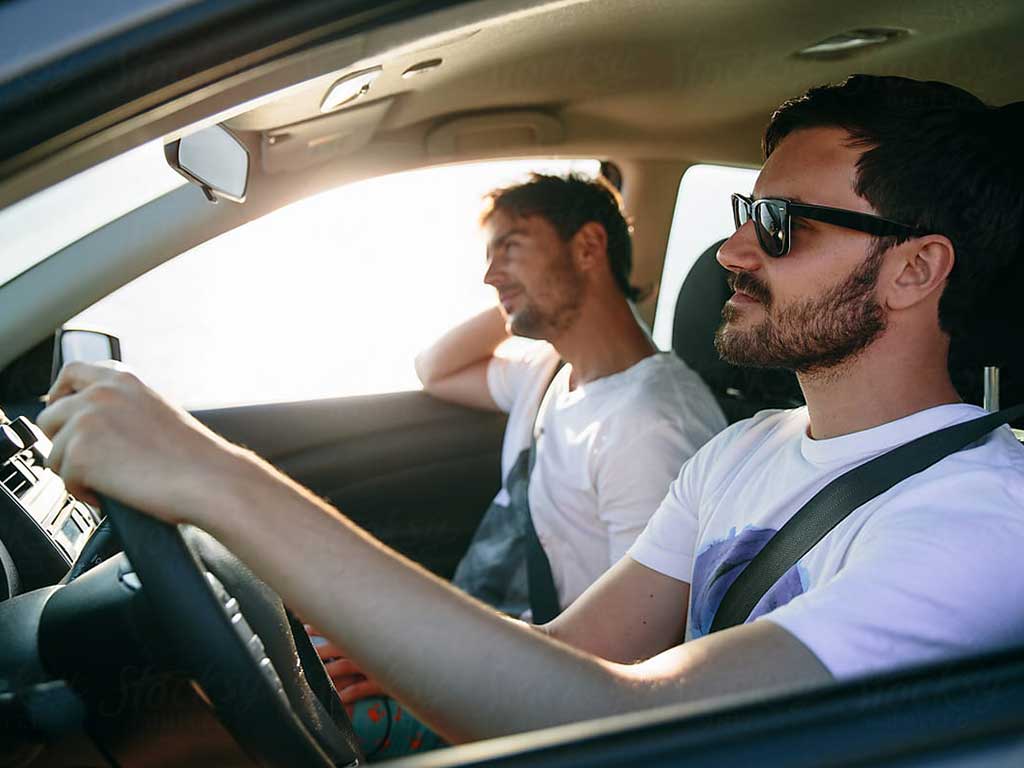 A man driving with sunglasses on with another man in the other seat