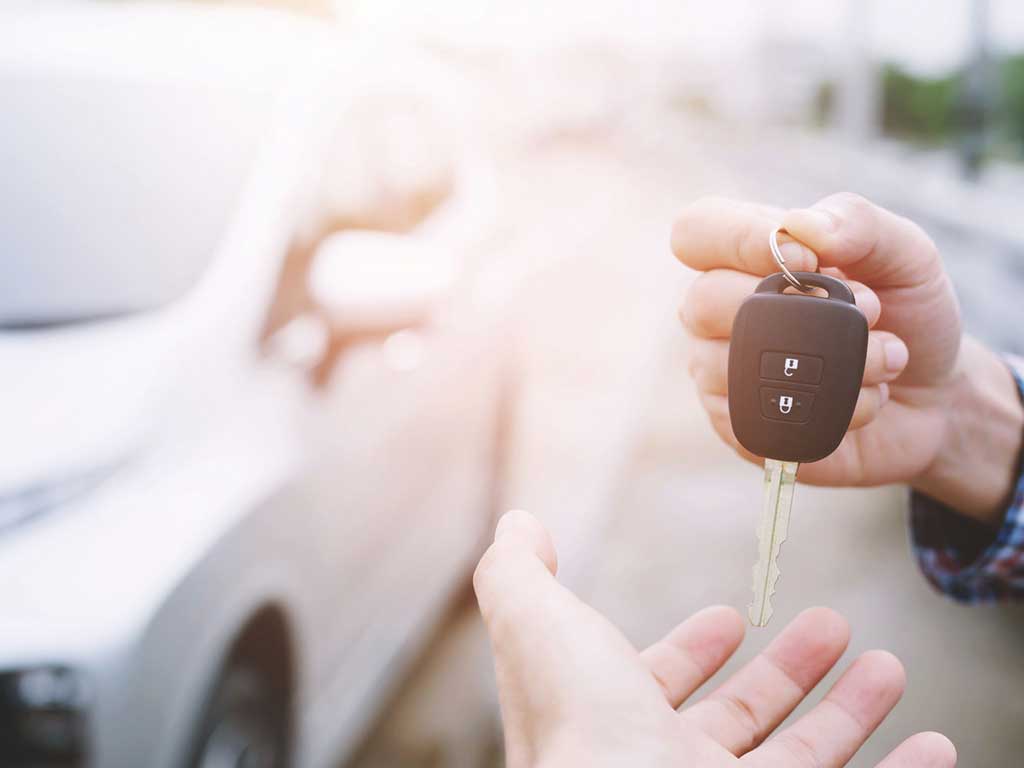 A person handing a car key to another person while outside