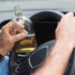 A person holding a bottle of alcohol while behind the wheel