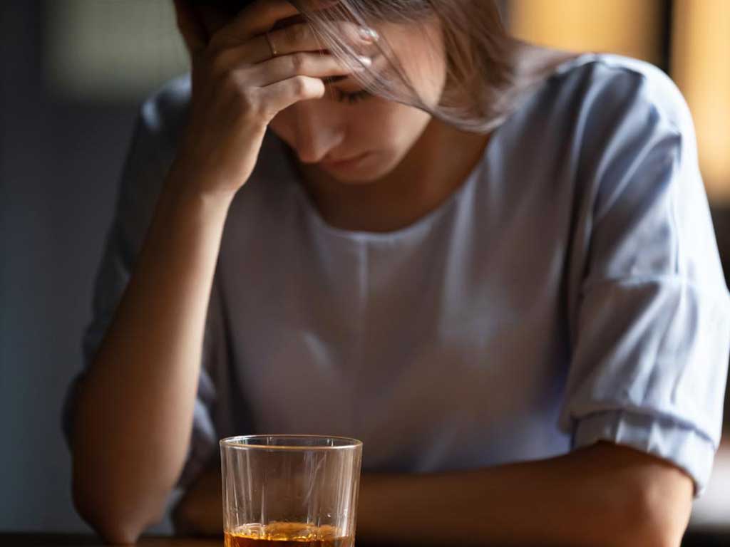 A woman looking distressed with a glass of alcohol in front of her