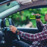 A man drinking beer while driving a car