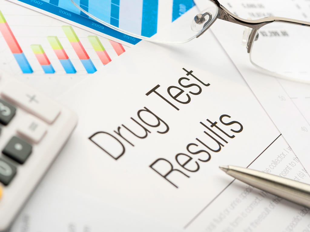 A paper containing the drug test results and a pen, eyeglass, and calculator in the background