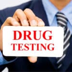 A person in corporate attire holding a "drug testing" sign