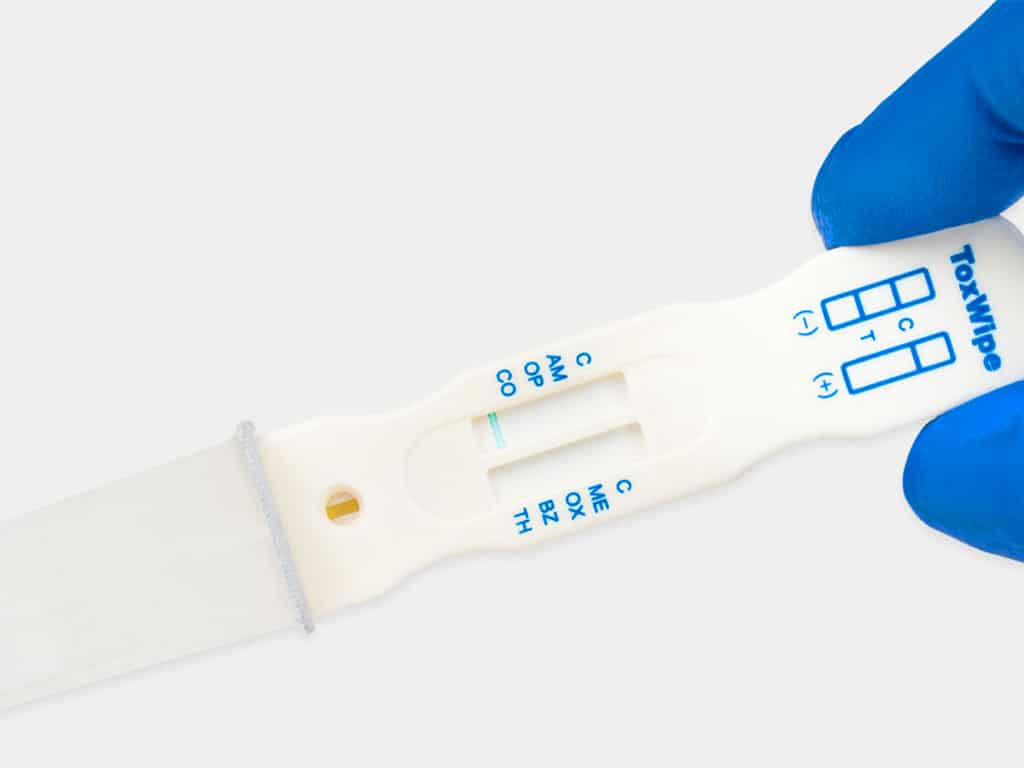A gloved hand holding a ToxWipe 7 saliva test kit