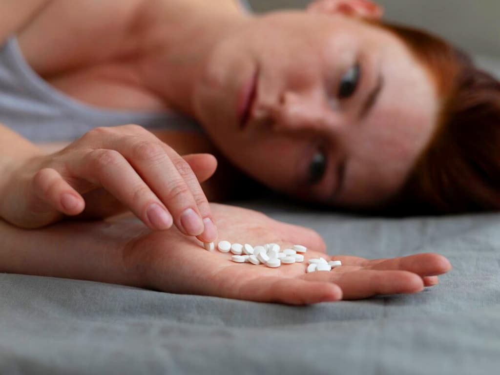 A woman lying on a bed, staring at her hand filled with drugs