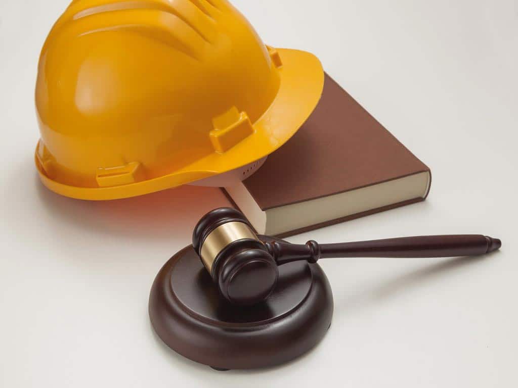 A gavel on a wooden sound block in front of a hard hat on a book