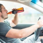 A male individual drinking beer while driving