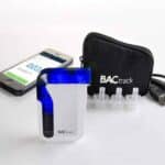 A BACtrack breathalyser near a smartphone, mouthpieces, and carry bag