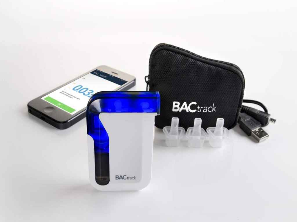 A BACtrack breathalyser near a smartphone, mouthpieces, and carry bag